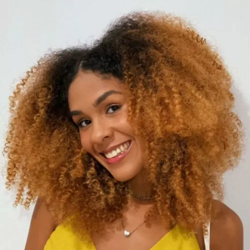 mulher negra de cabelo crespo loiro. Ela veste blusa amarela.