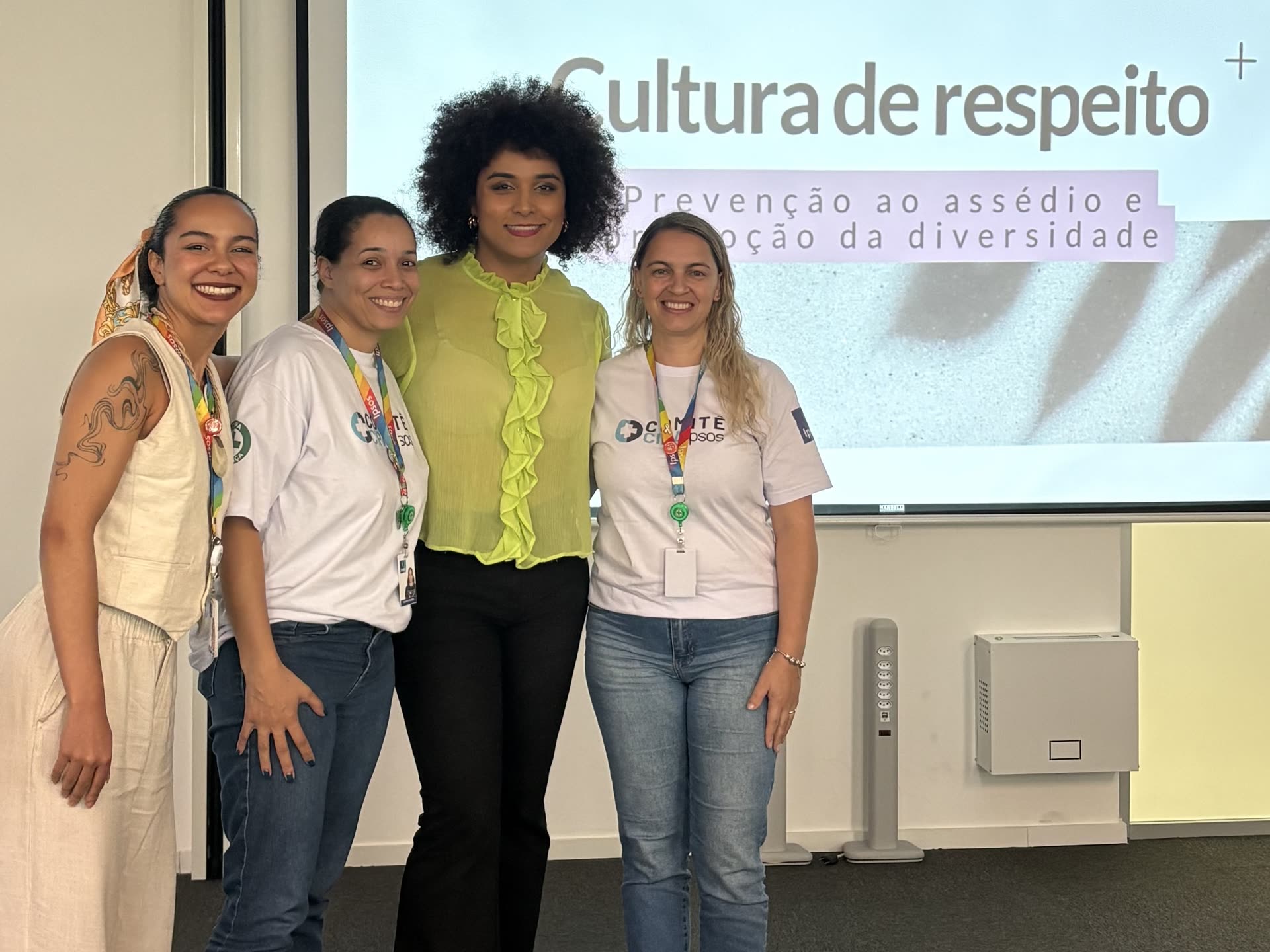 Gabriela Augusto ao lado de mulheres da Ipsos, com tela ao fundo projetando 'Cultura de respeito: prevenção ao assédio e promoção da diversidade'
