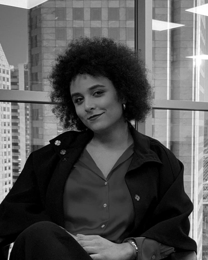 Retrato em preto e branco de Gabriela Augusto sentada diante de uma janela, com vista da Ponte Estaiada de São Paulo