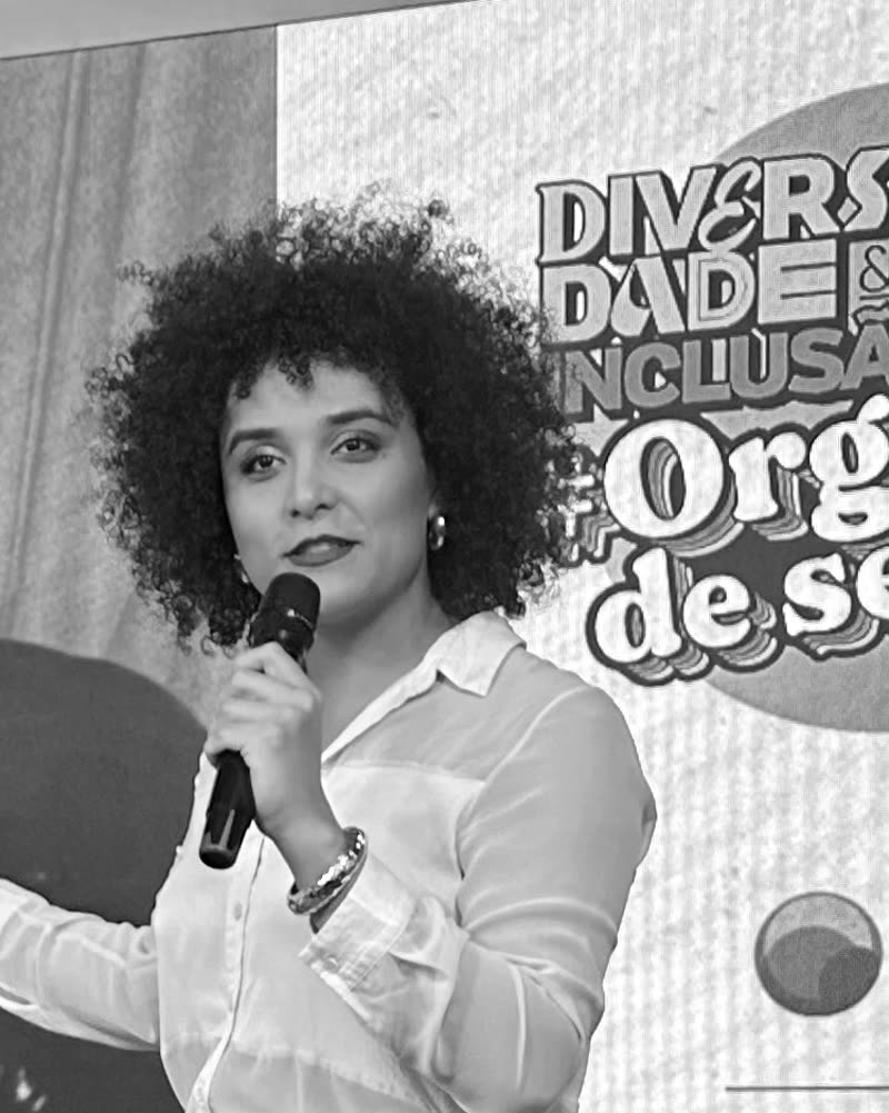 Retrato em preto e branco de Gabriela Augusto com microfone, palestrando no evento Diversidade & Inclusão #Orgulho de ser EU
