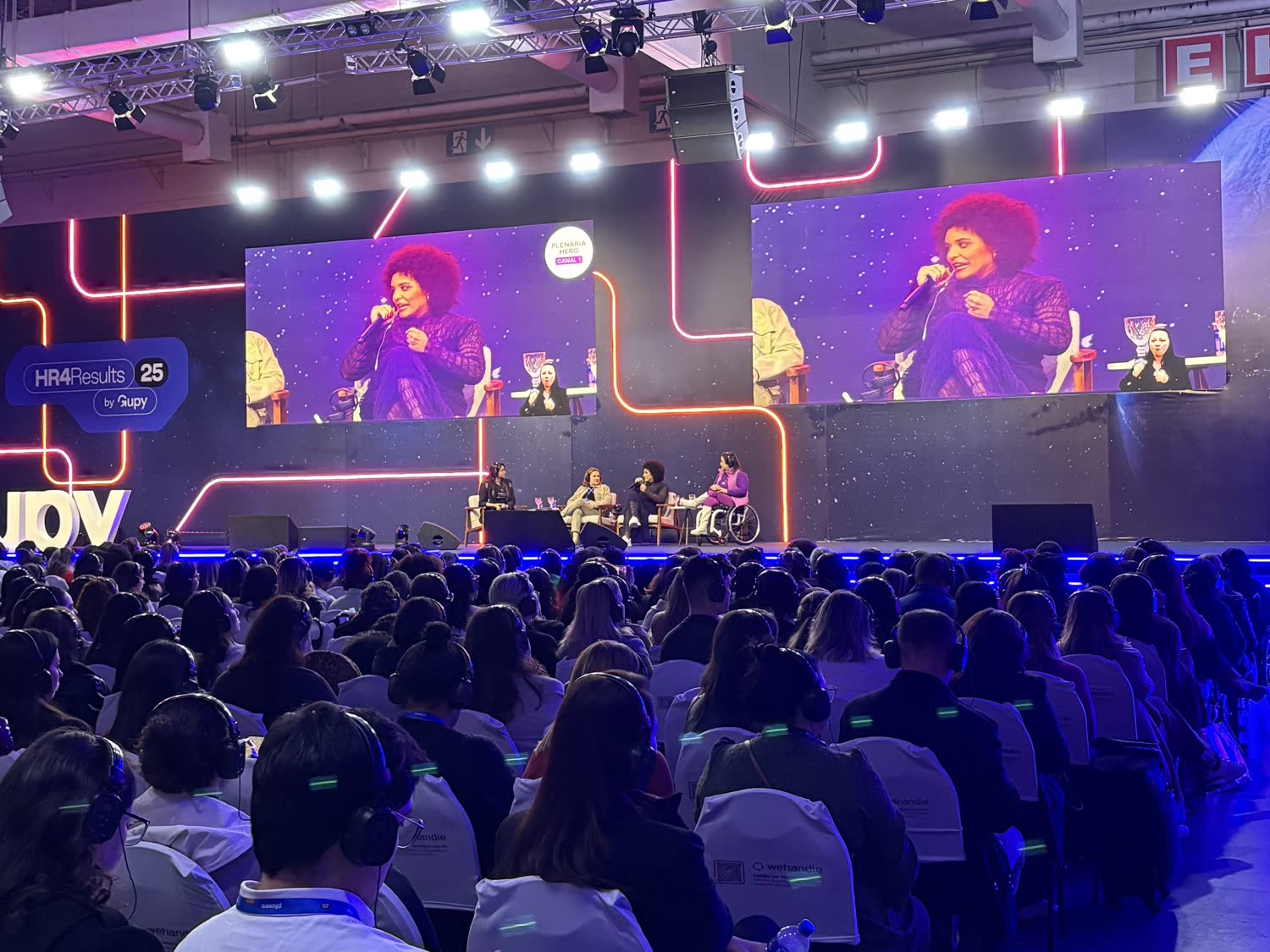 Auditório lotado durante o evento HR4Results, da Gupy, com duas telas exibindo Gabriela Augusto no palco