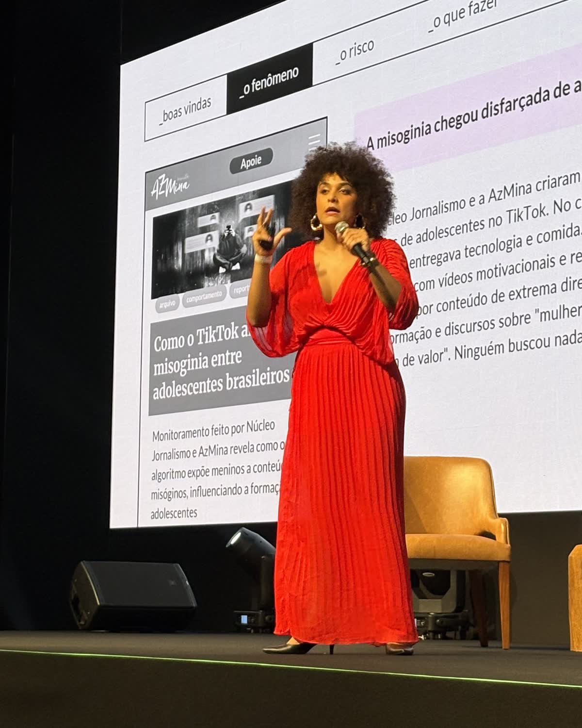 Gabriela Augusto gesticula durante uma palestra, com telão ao fundo exibindo conteúdo sobre misoginia e redes sociais
