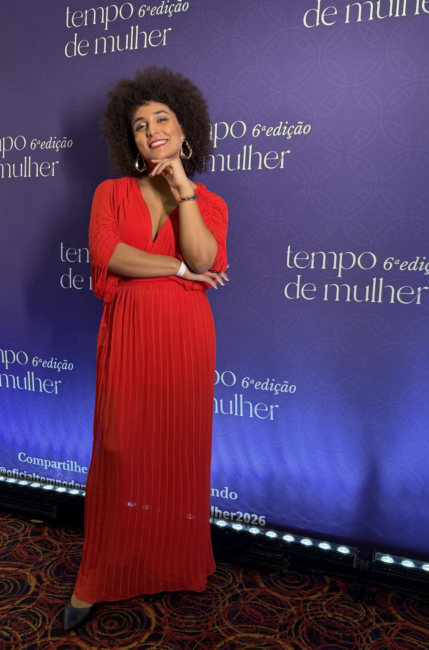 Gabriela Augusto de vestido vermelho longo, sorrindo diante do painel do evento Tempo de Mulher